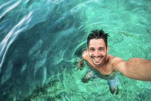 A man standing in clear blue water whilst taking a selfie.